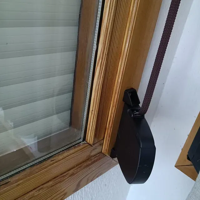 Marco de ventana de madera marrón con un mecanismo de control de persiana negro y una persiana a rayas blancas y beige.