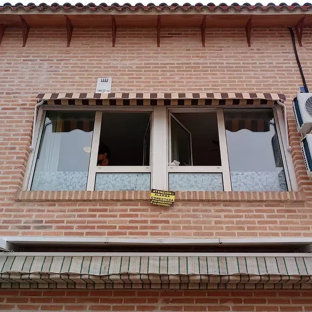 Edificio de ladrillo con toldo sobre las ventanas; una ventana abierta.