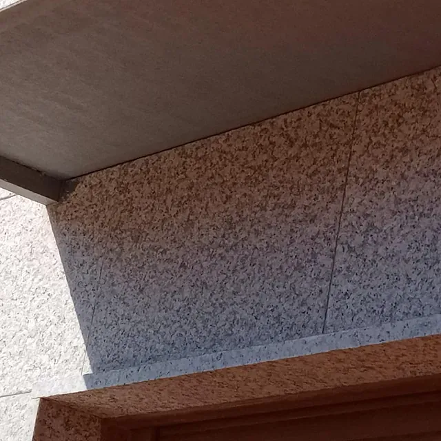 Primer plano de una pared de estuco texturizado debajo de un voladizo de hormigón, con un marco de puerta de madera visible.