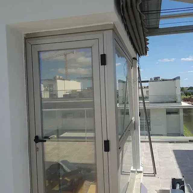 Puerta y ventana de cristal en un balcón con vistas a los edificios y al cielo azul.