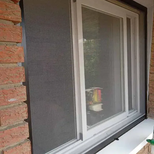 Ventana corredera blanca con mosquitera instalada en una pared de ladrillo.