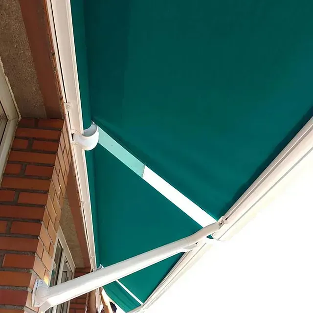 Toldo verde que se extiende desde un edificio de ladrillo, con soportes blancos.