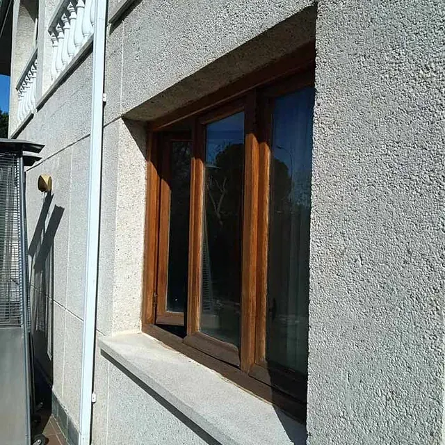 Ventana marrón en la fachada texturizada de un edificio gris claro. Un cristal está abierto.