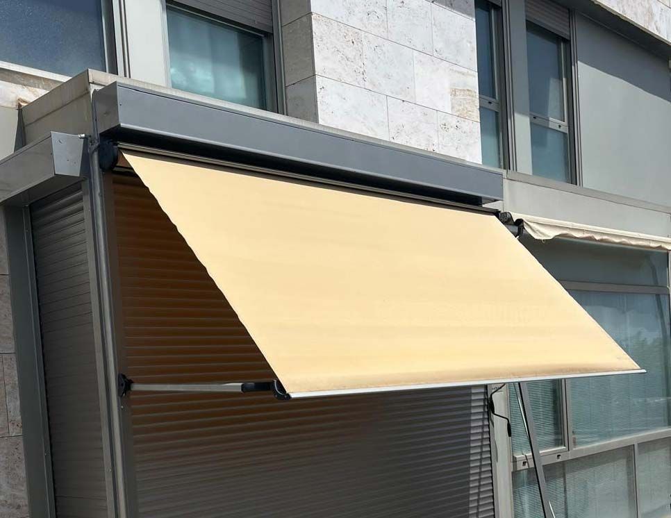 Un toldo color beige se extendía desde un edificio, cubriendo parcialmente una ventana.