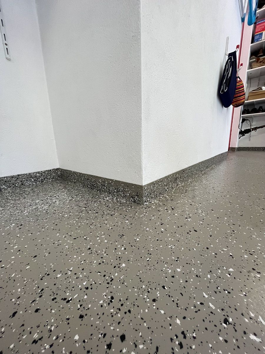 Eine Zimmerecke mit grauem Boden und weißen Wänden.