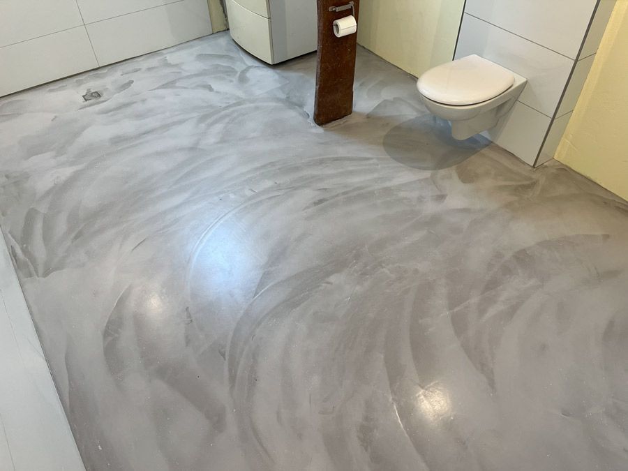 Ein Badezimmer mit Betonboden und Toilette.