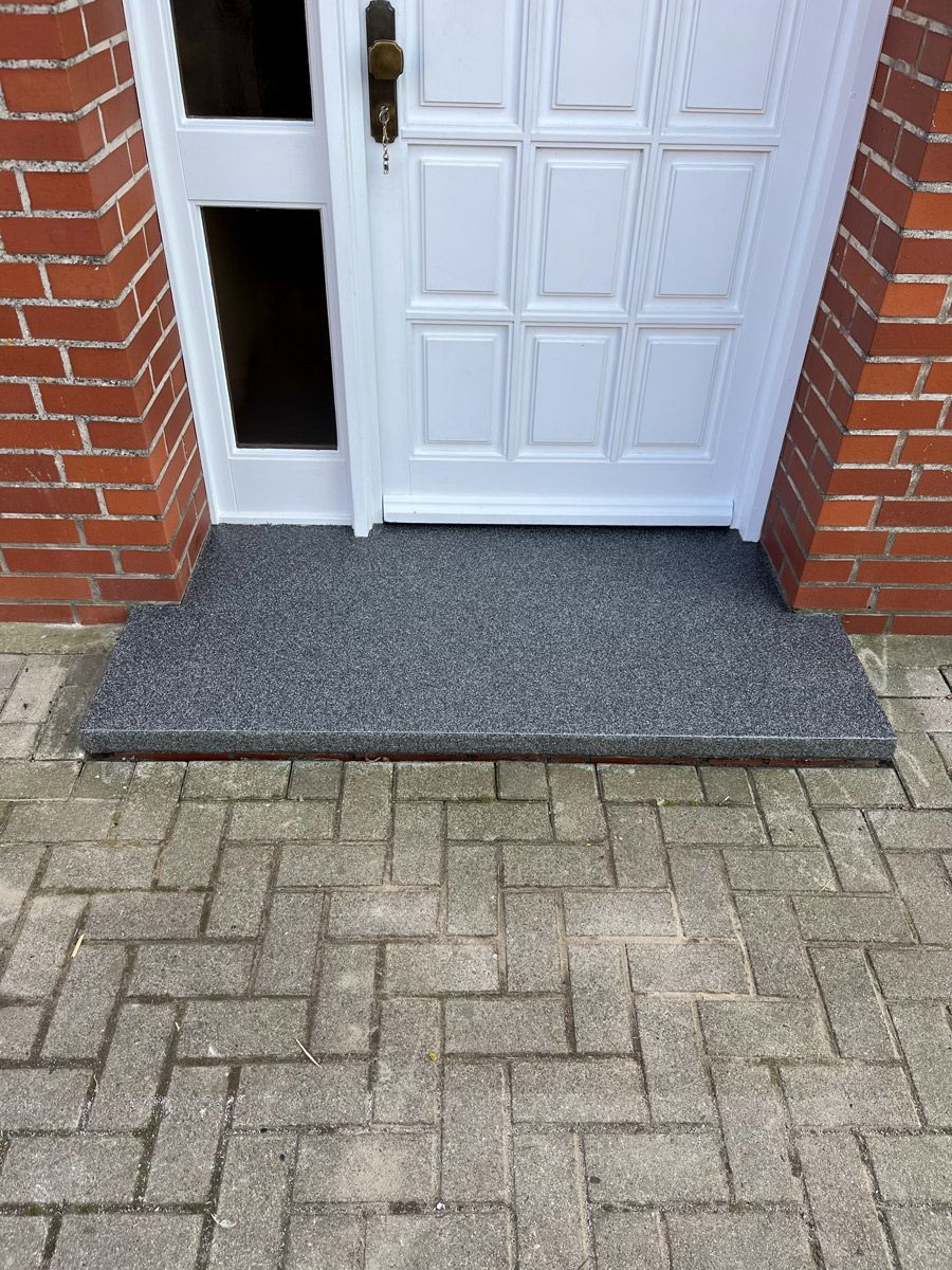 Auf einem gemauerten Gehweg neben einer Ziegelmauer steht eine weiße Tür.