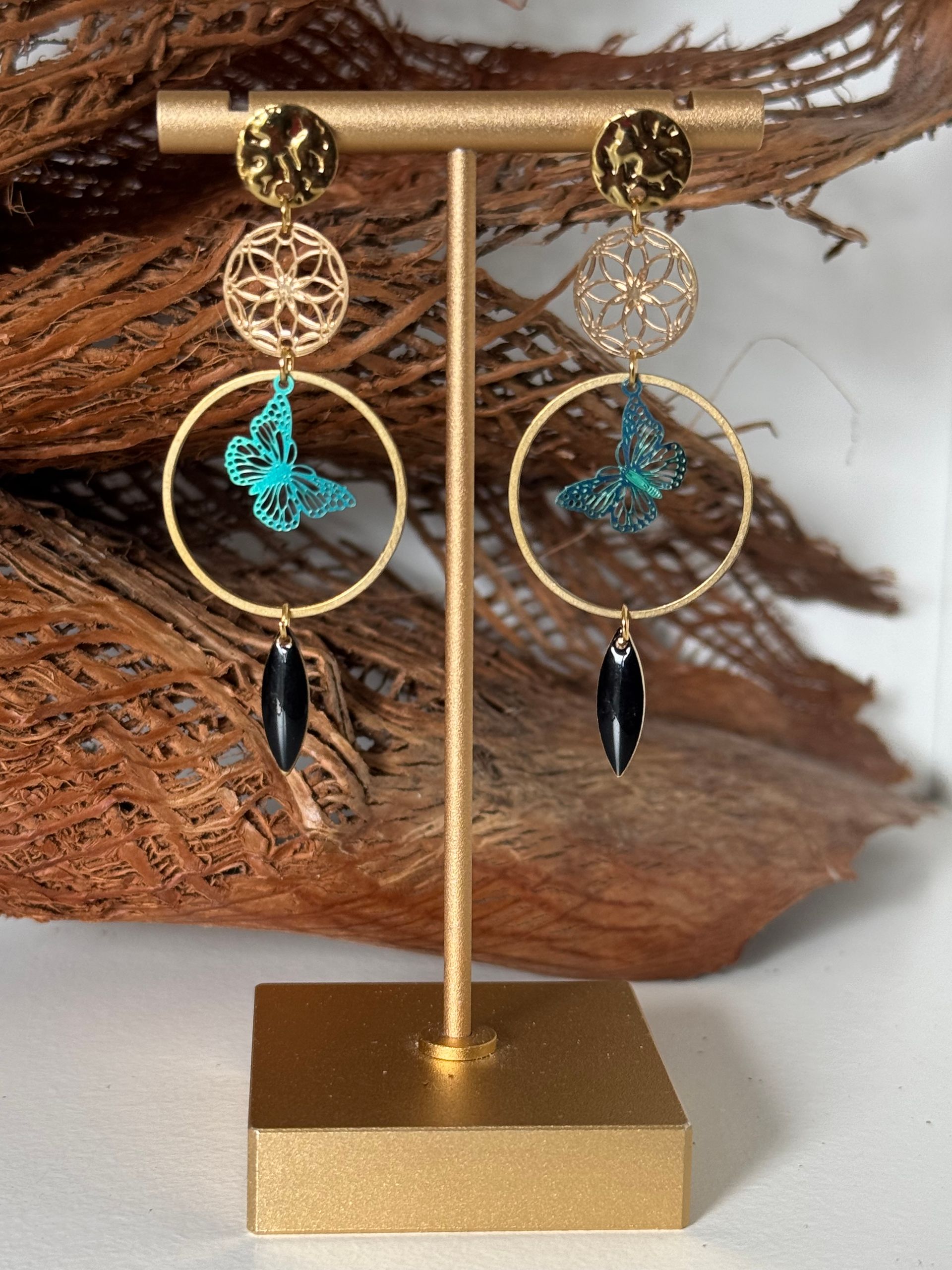 Boucles d'oreilles en or exposées. Chacune est ornée d'un pendentif en forme de disque, de cercle, de papillon et de perle noire.