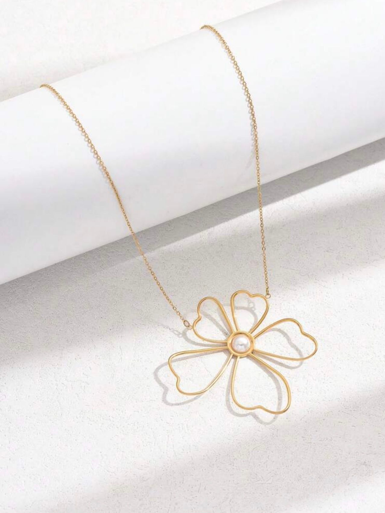 Collier avec pendentif fleur dorée sur fond blanc.