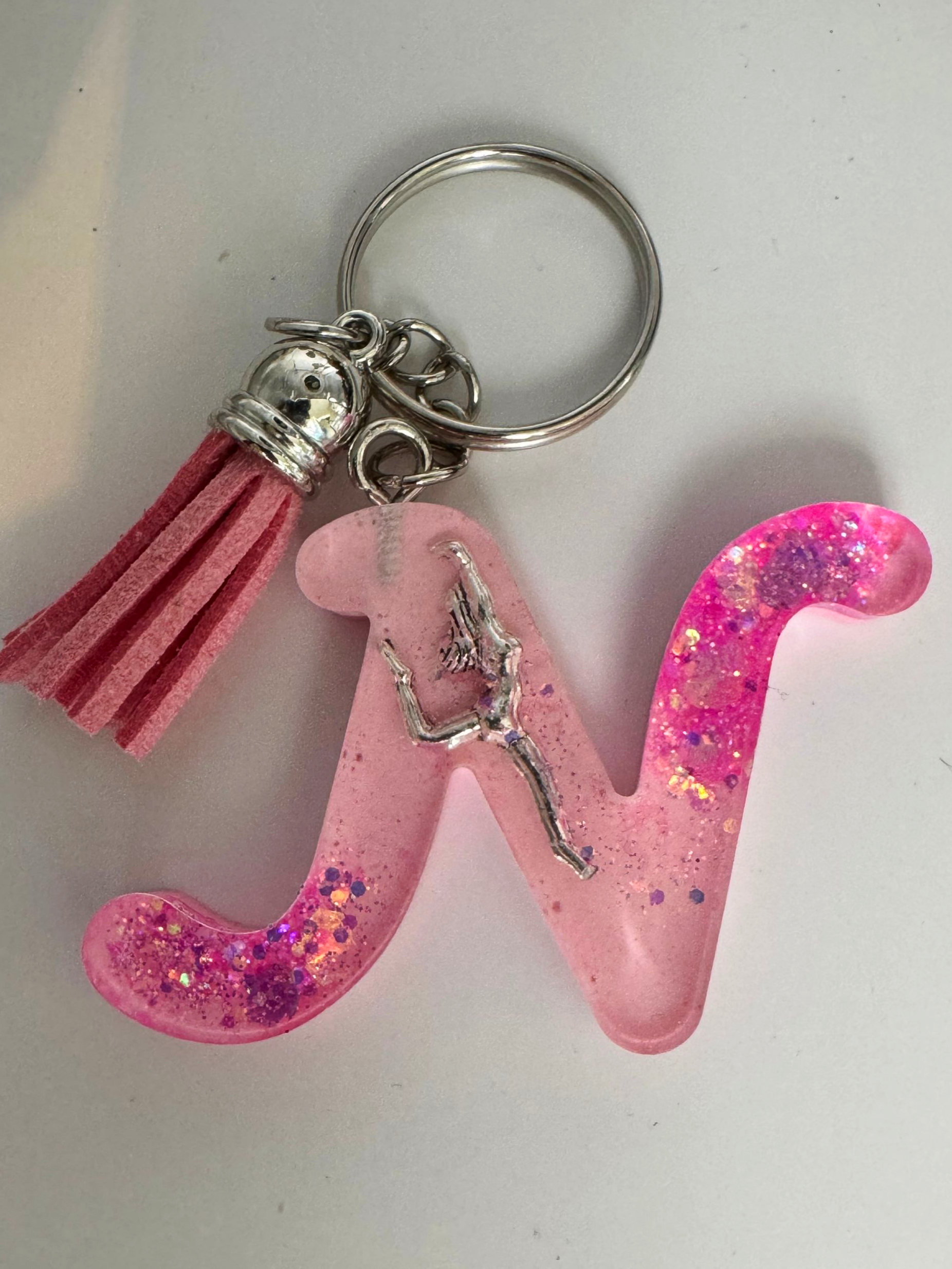Porte-clés en forme de lettre N rose à paillettes, avec une danseuse argentée et un pompon rose.