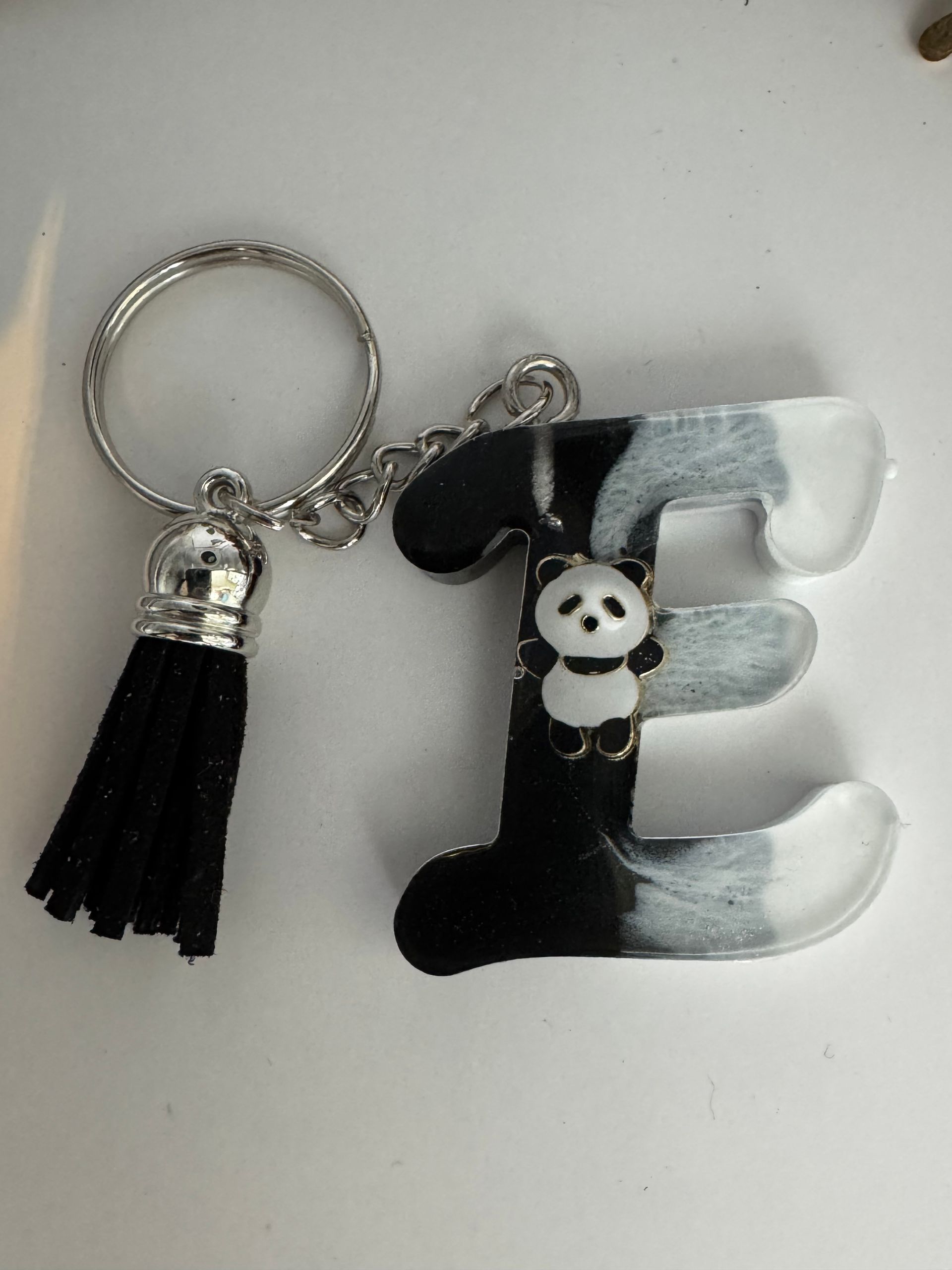 Porte-clés lettre E  en résine noire, blanche et grise avec un panda, un pompon noir et des finitions argentées.