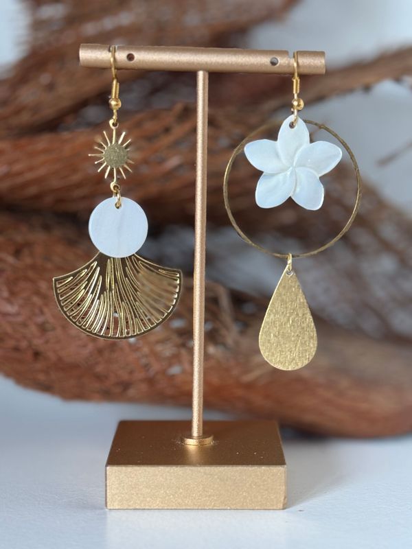 Boucles d'oreilles asymétriques en or, ornées de motifs soleil, éventail, cercle et larme, présentées sur un présentoir.