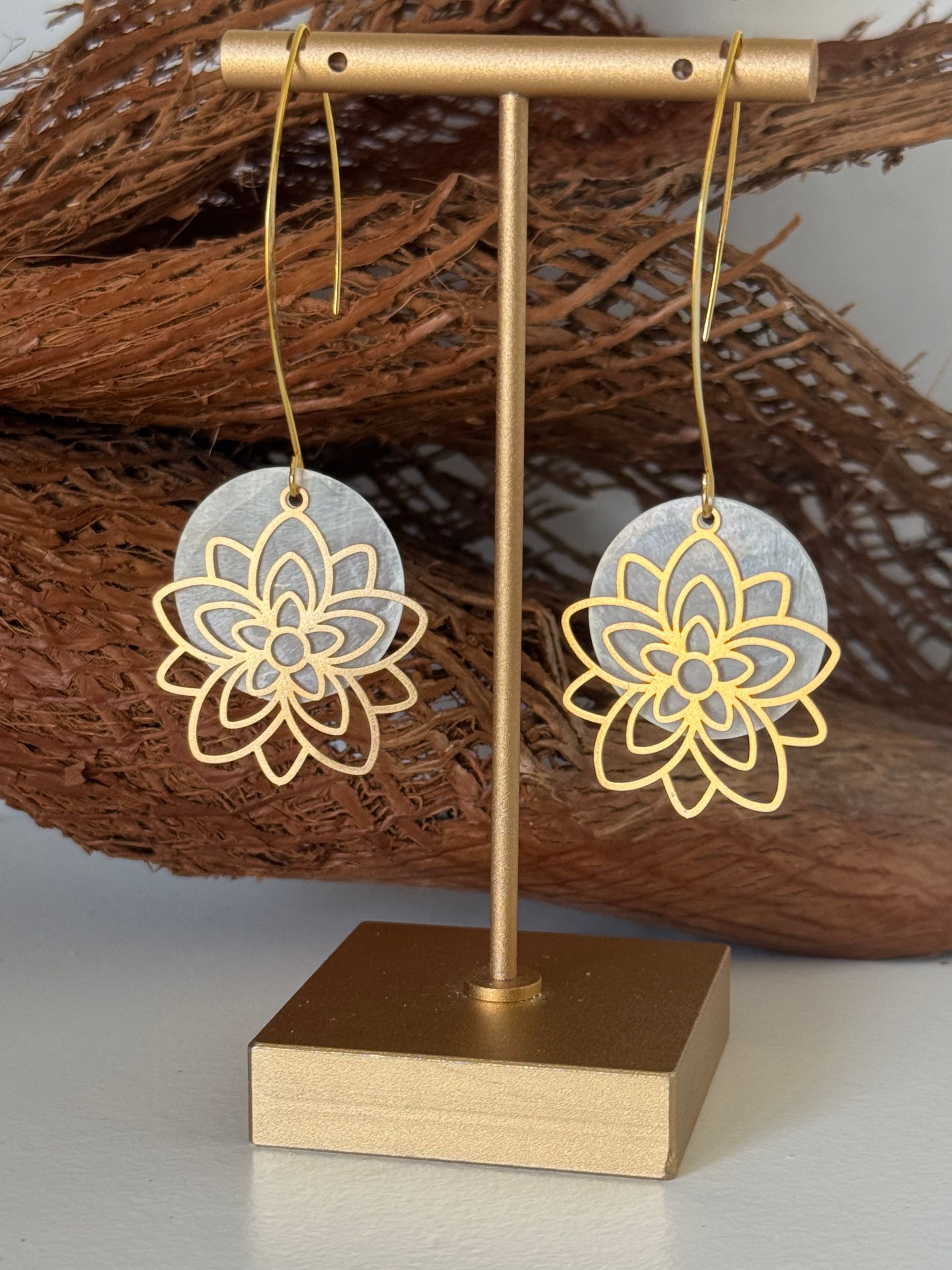 Boucles d'oreilles en or à motif floral, présentées sur un support en or, sur un fond texturé brun.