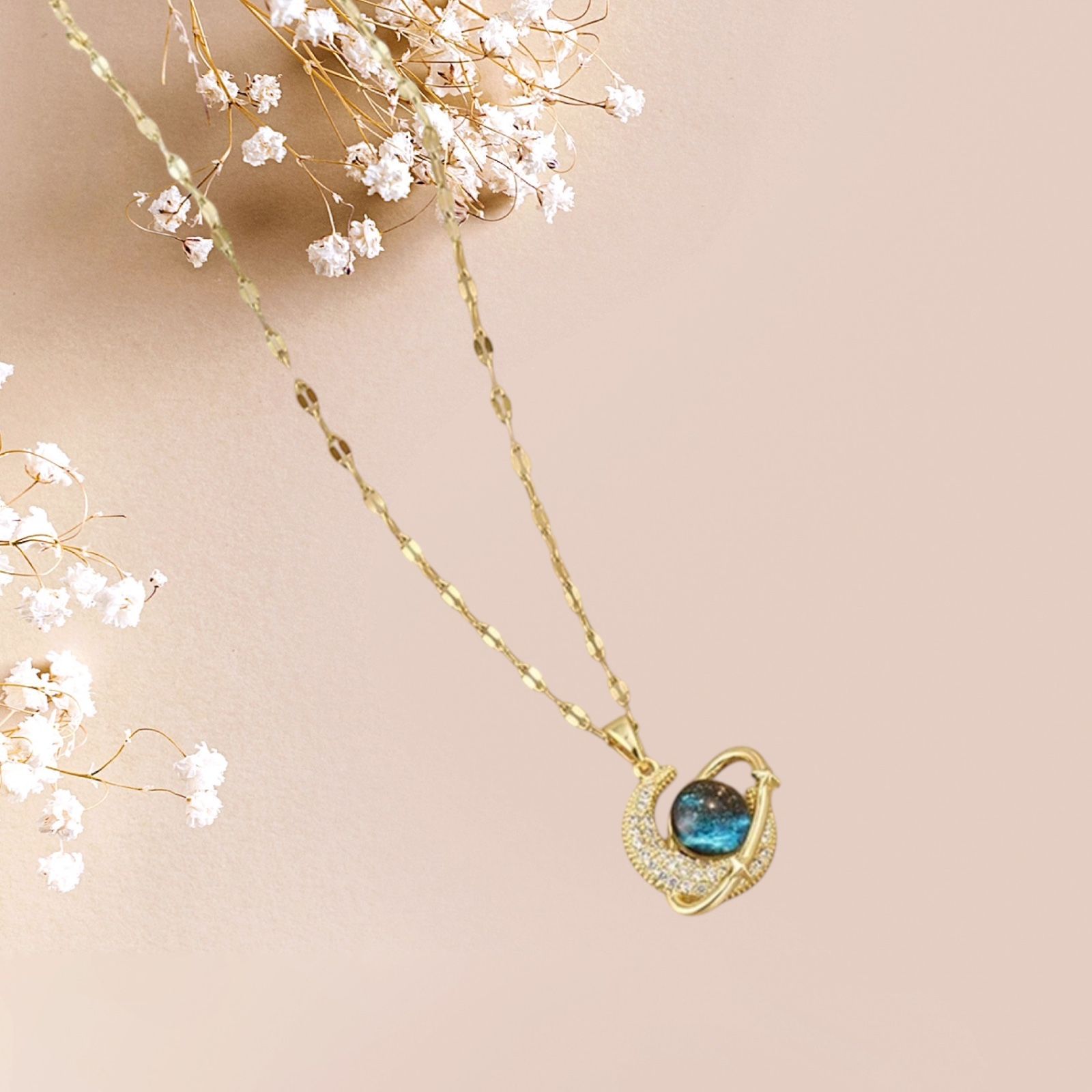 Collier en or avec un pendentif en pierre  bleue, entouré de petits cristaux, sur fond rose.