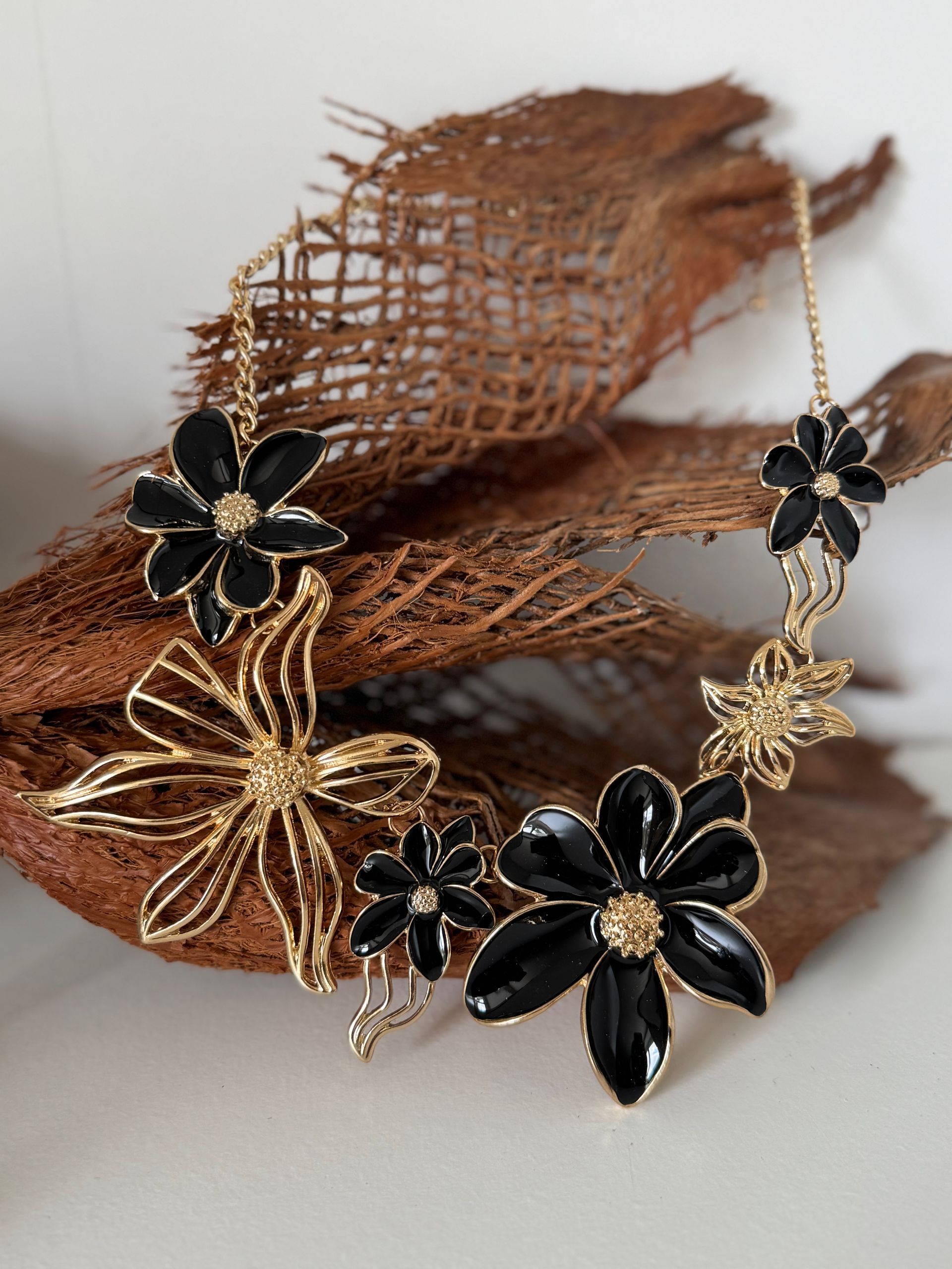 Collier floral doré et noir sur une surface texturée brune.