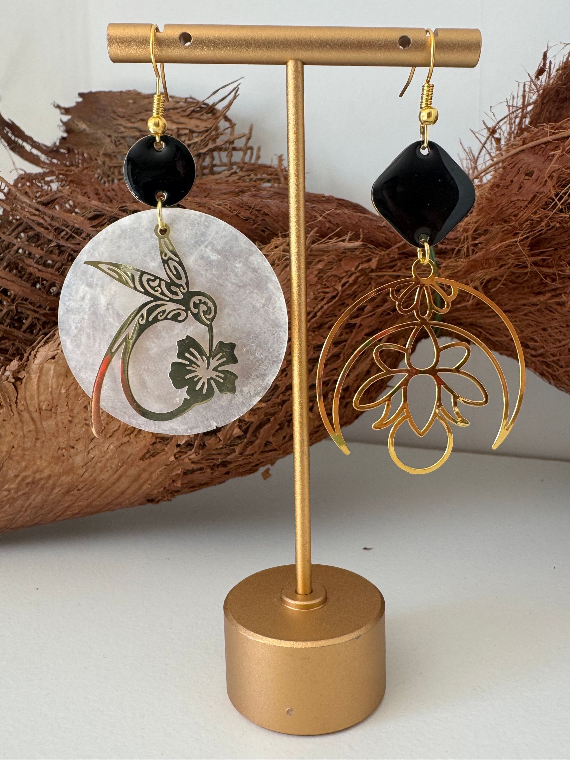Présentoir à boucles d'oreilles en or avec deux boucles d'oreilles asymétriques, l'une circulaire avec un colibri, l'autre géométrique.