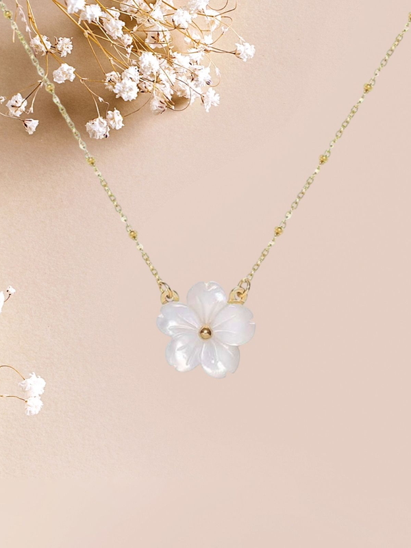 Collier en or avec un pendentif en forme de fleur blanche sur fond rose, orné de fleurs blanches.