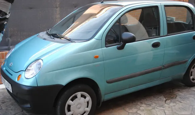 Un pequeño coche azul está aparcado al costado de la carretera.