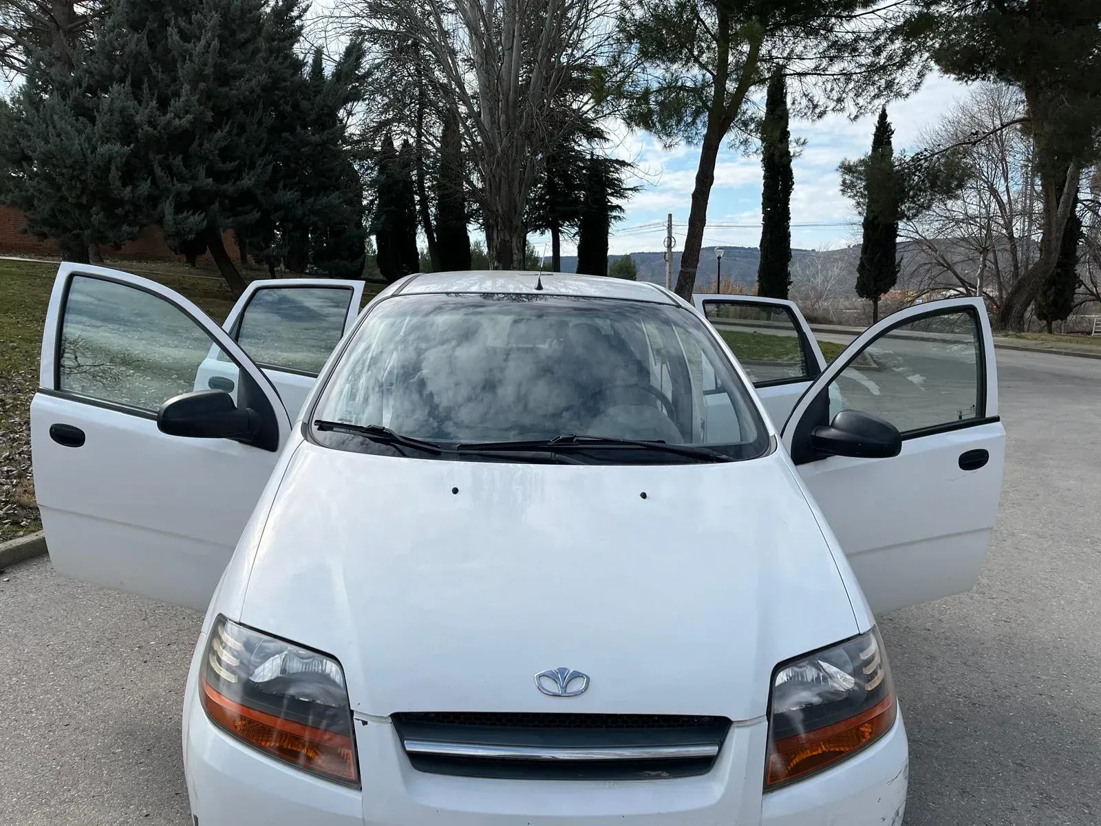 Un coche blanco con las puertas abiertas está estacionado al costado de la carretera.