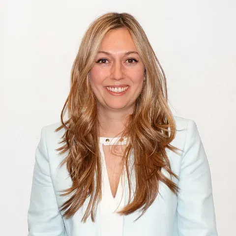 Una mujer que lleva una chaqueta azul claro y una camisa blanca sonríe a la cámara.