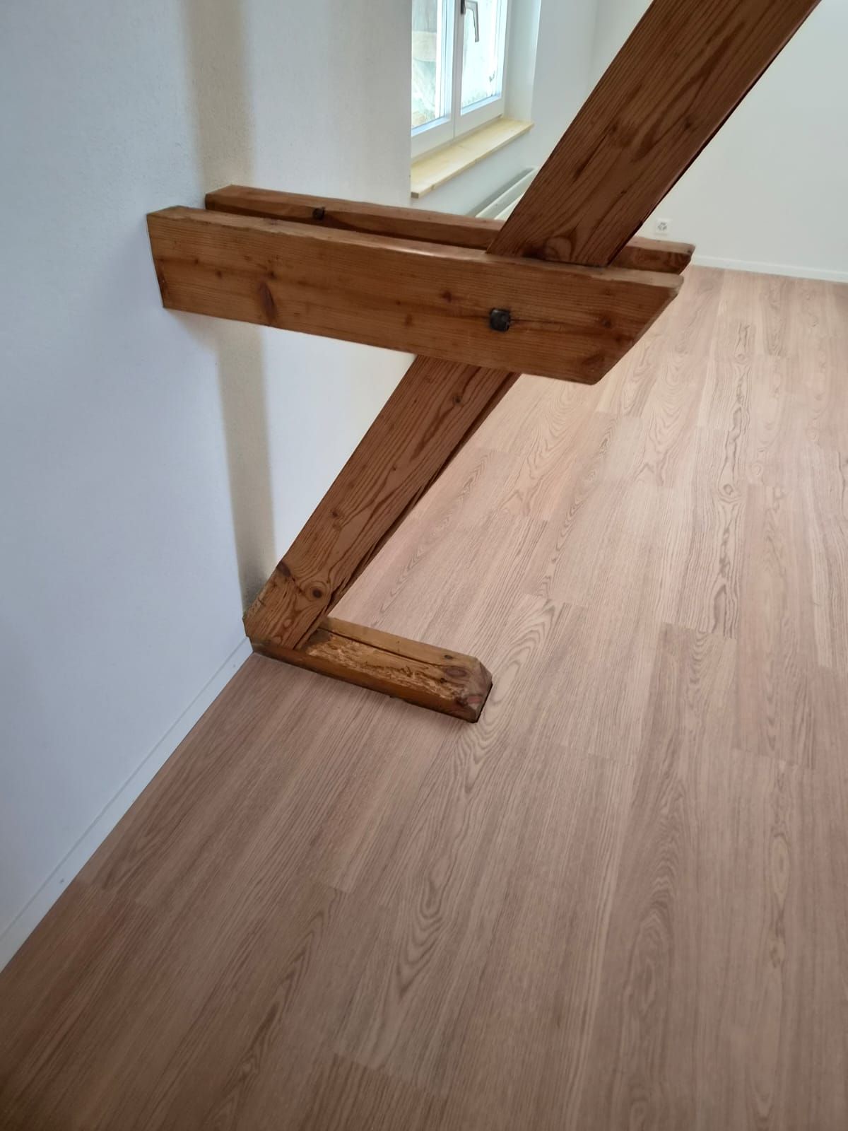 Holztreppenstützbalken auf hellem Holzboden in der Nähe eines Fensters und einer weissen Wand