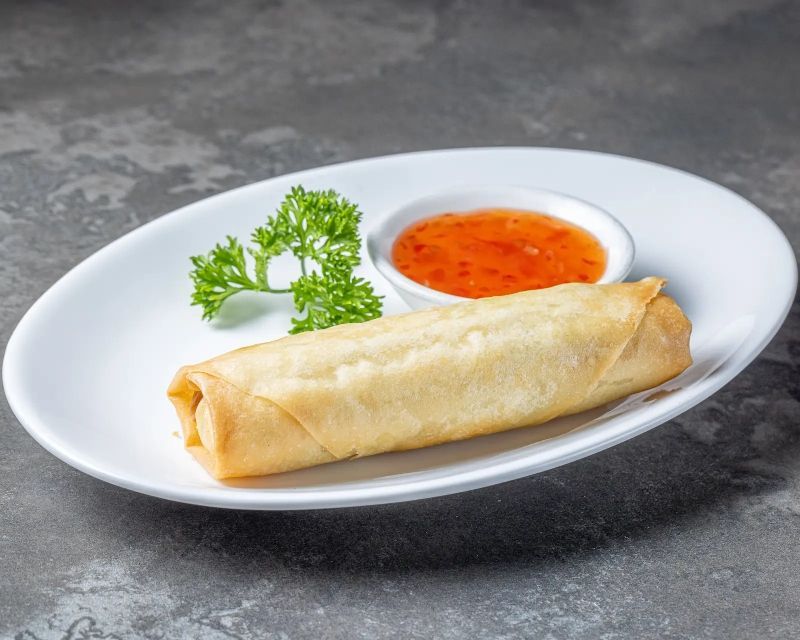 Un rouleau de printemps avec une sauce à tremper sur une assiette blanche.