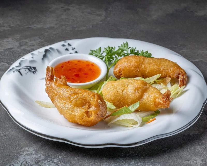 Une assiette blanche garnie de crevettes frites et d'un petit bol de sauce à tremper.