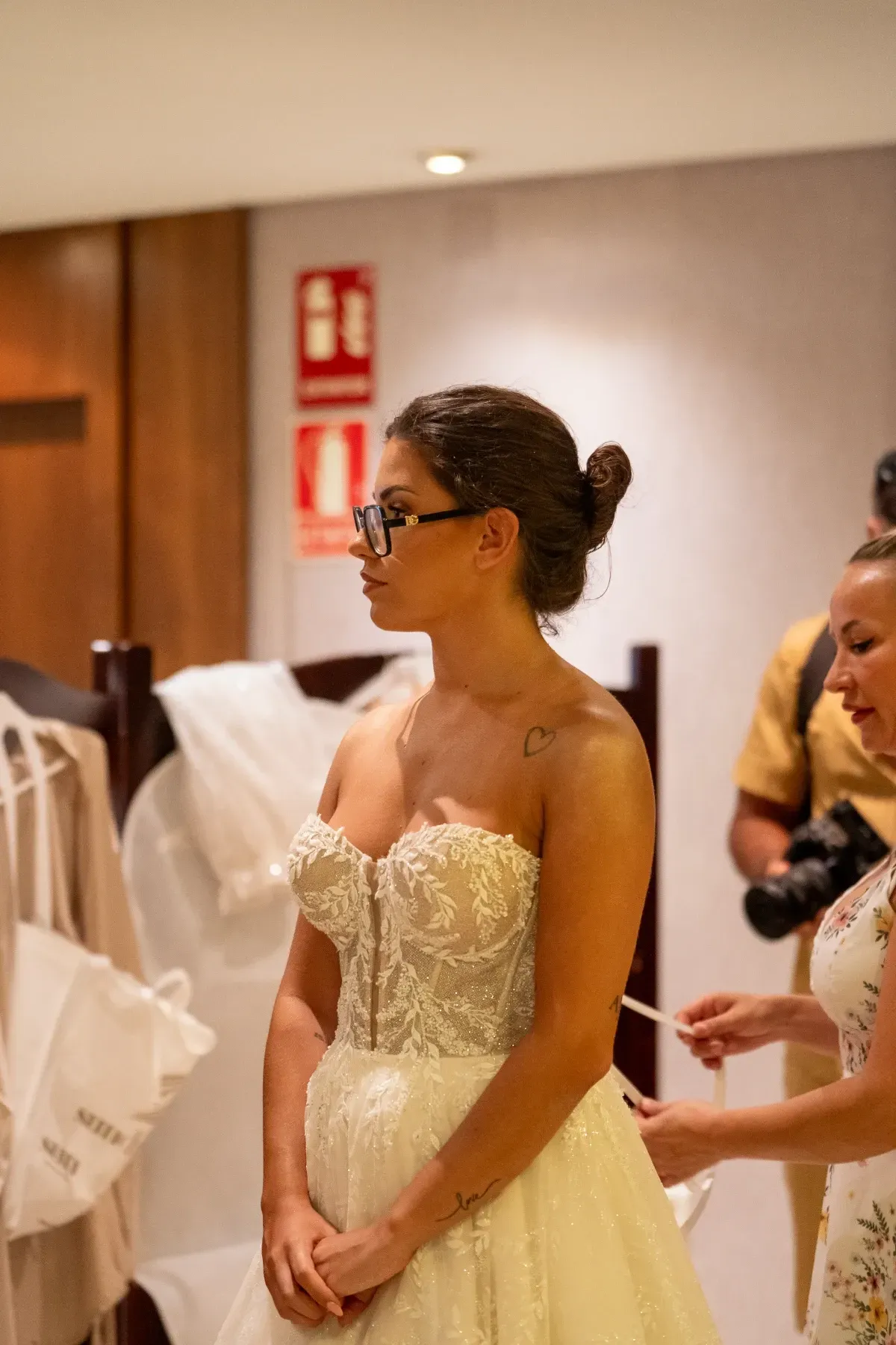 Novia con vestido de novia con corpiño de corsé; alguien le ajusta el vestido.