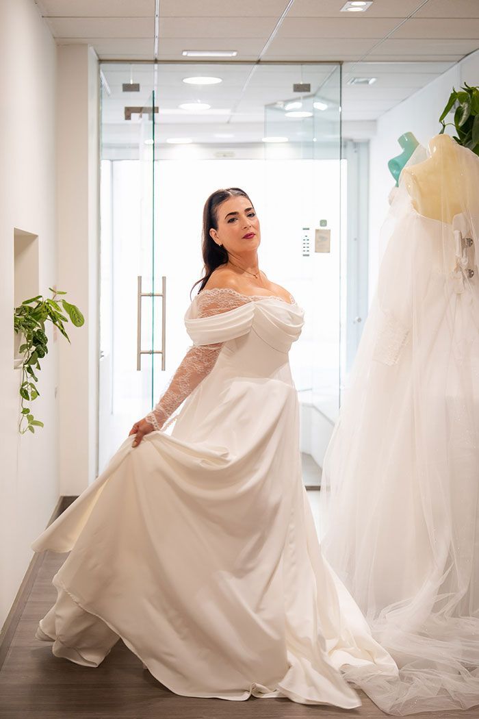 Mujer con vestido de novia blanco, sosteniendo falda, en una tienda de novias.