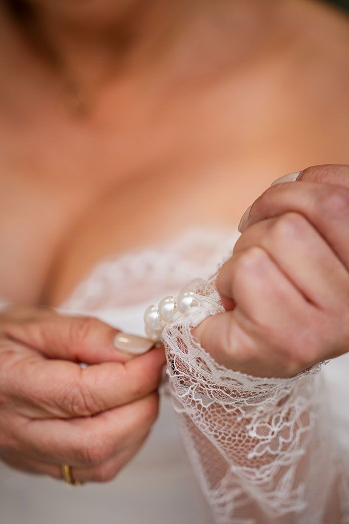 Manos ajustando una manga de encaje blanco adornada con perlas, cerca de un escote.