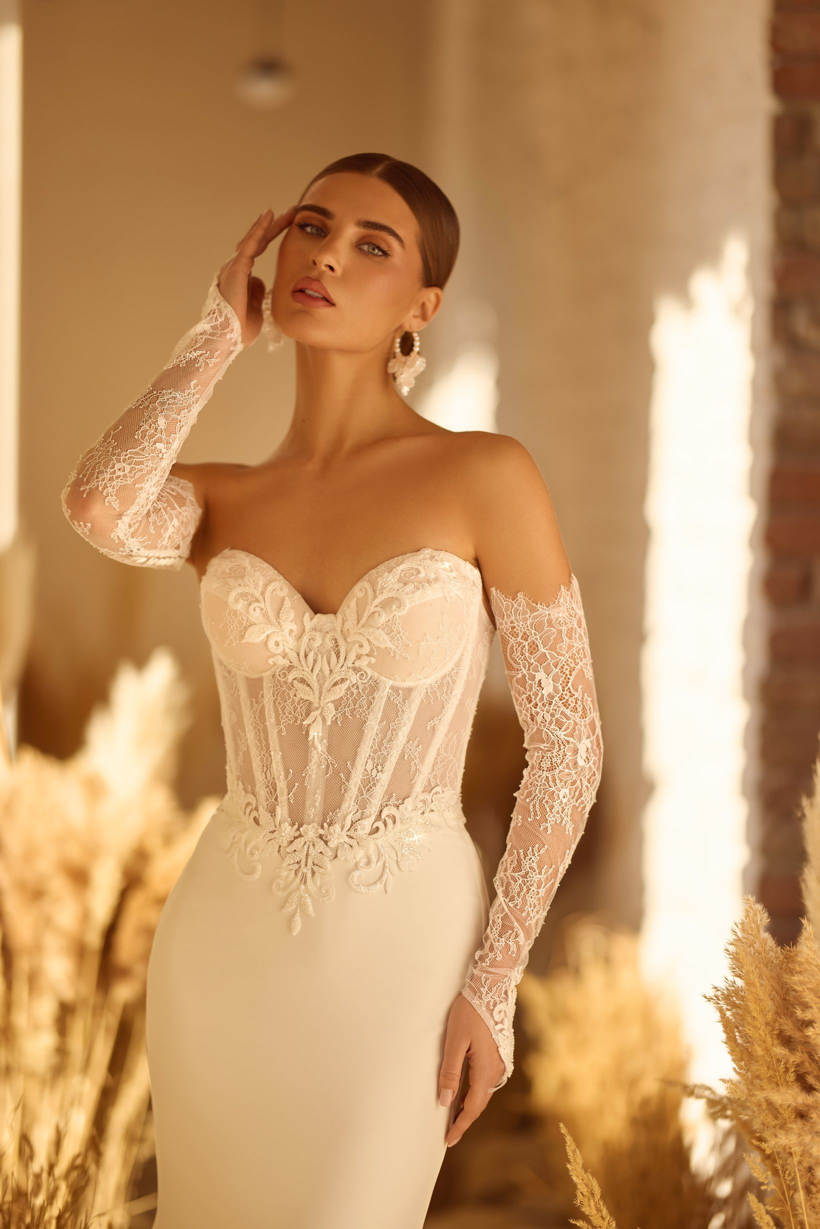 Mujer con un vestido de novia blanco con mangas y corpiño de encaje, posando.