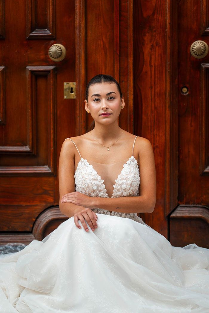Una mujer con vestido de novia se sienta en los escalones frente a una gran puerta de madera.