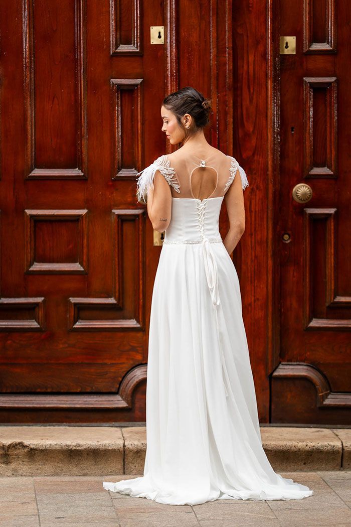 Una mujer con un vestido de novia blanco se encuentra frente a una gran puerta de madera ornamentada.