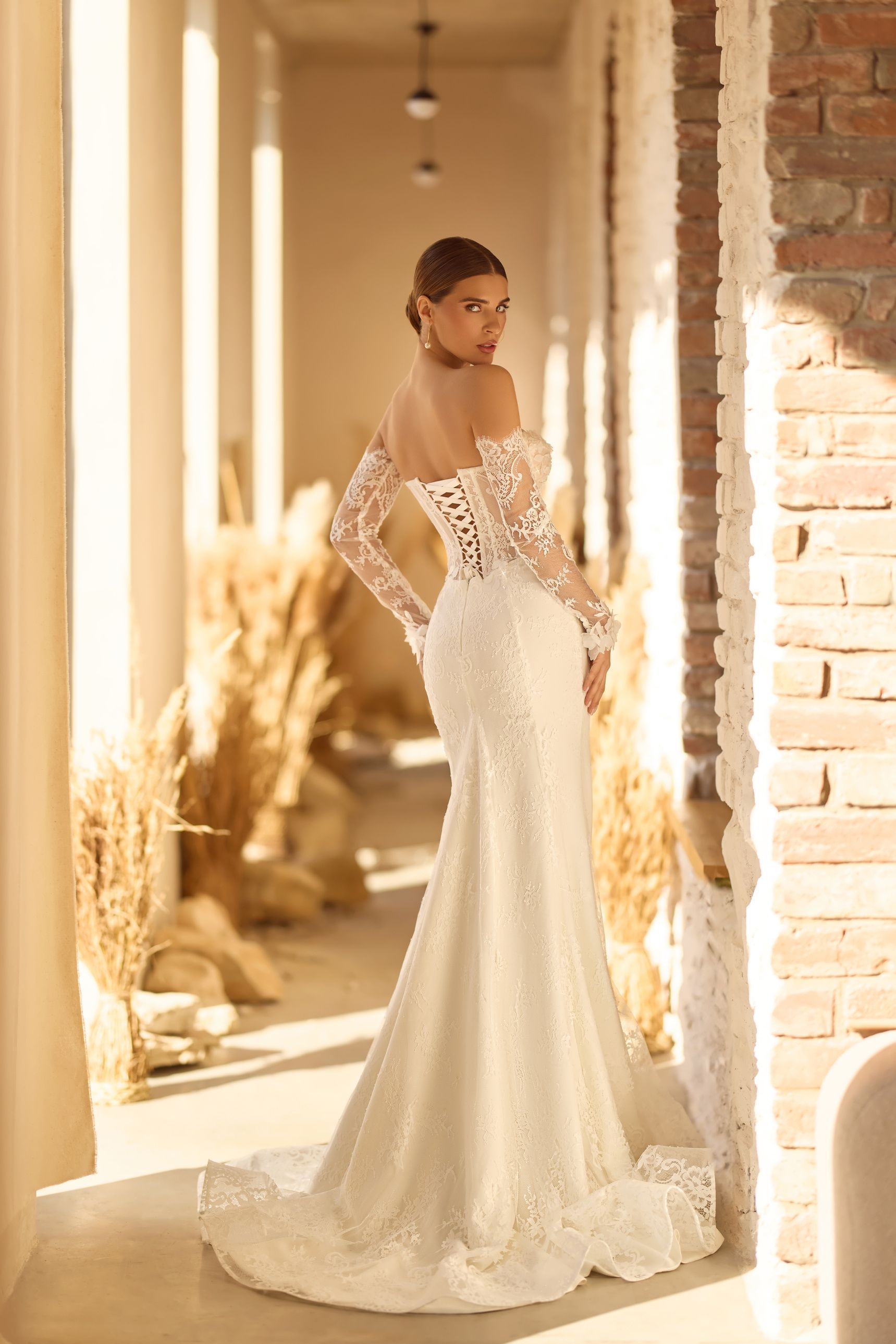 Mujer con un vestido de novia de encaje blanco, de pie en un interior soleado.