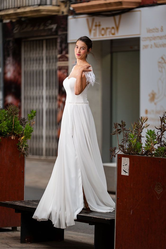 Mujer con vestido de novia blanco con detalles de plumas, posando al aire libre.