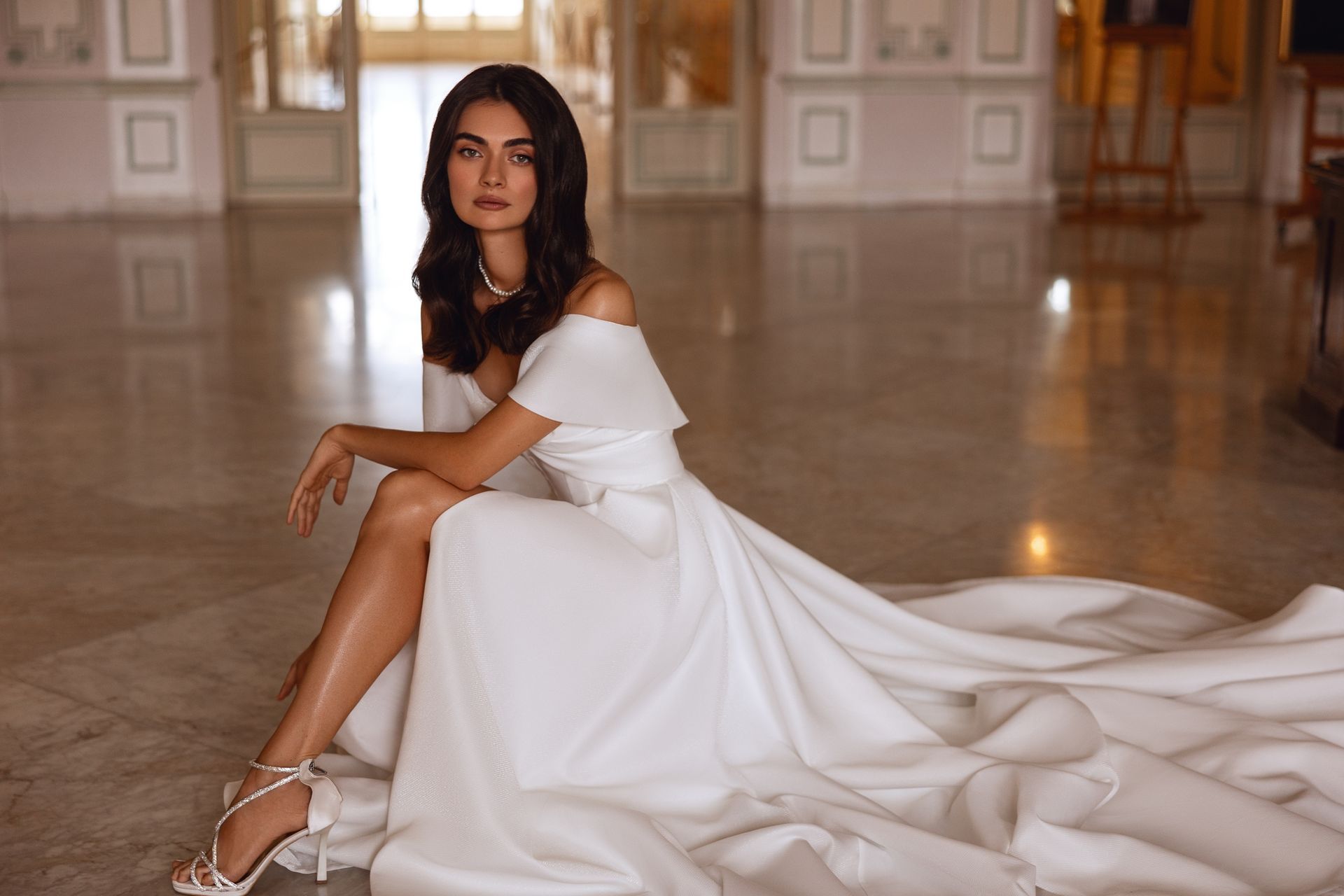 Mujer vestida de blanco, sentada, mirando a la cámara. Interior, suelo de mármol.