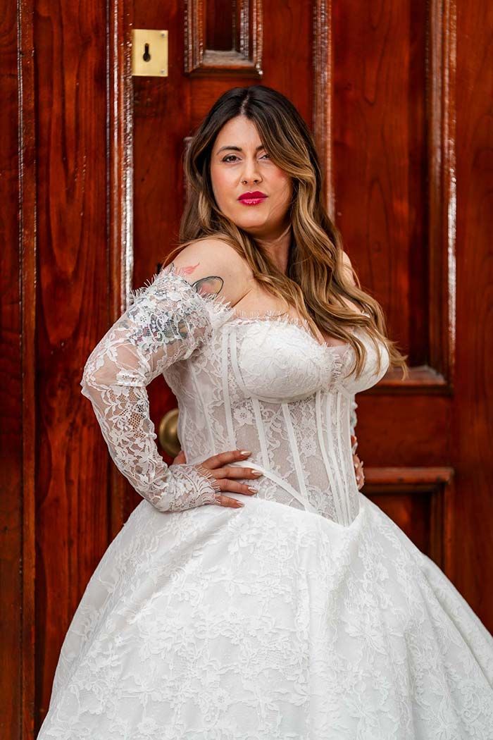 Mujer con un vestido de novia blanco con mangas de encaje, posando frente a una puerta de madera.