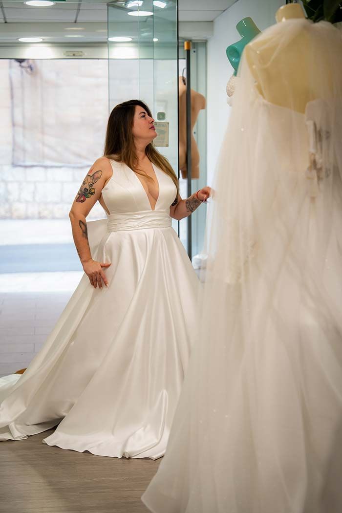 Una mujer con un vestido de novia blanco admira un vestido en un maniquí en una tienda de novias.