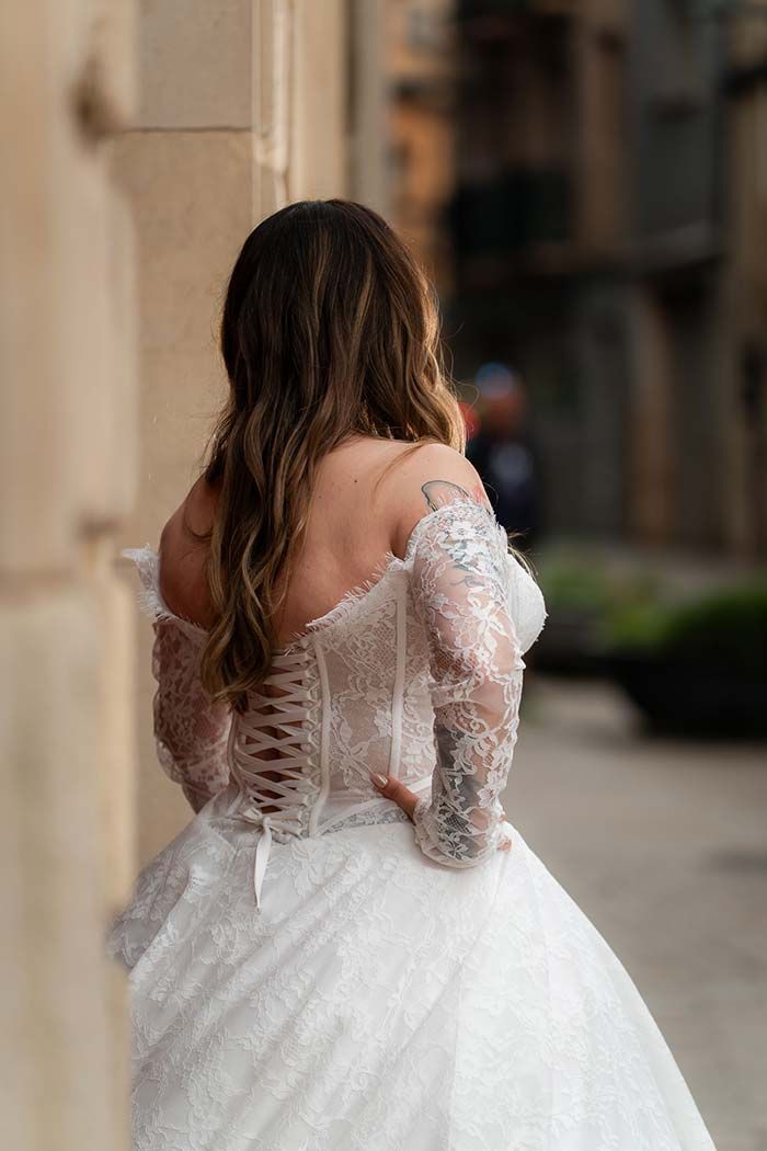 Novia con vestido de novia de encaje blanco, de pie al aire libre, de espaldas a la cámara.