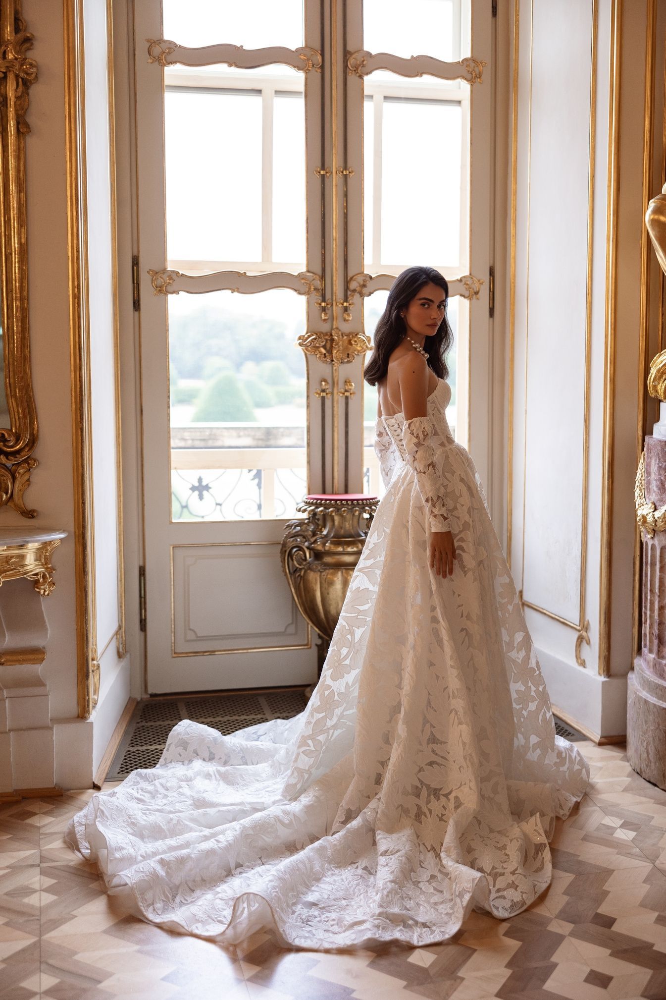 Una mujer con un vestido de novia de encaje se encuentra en una puerta dorada, mirando por encima del hombro.