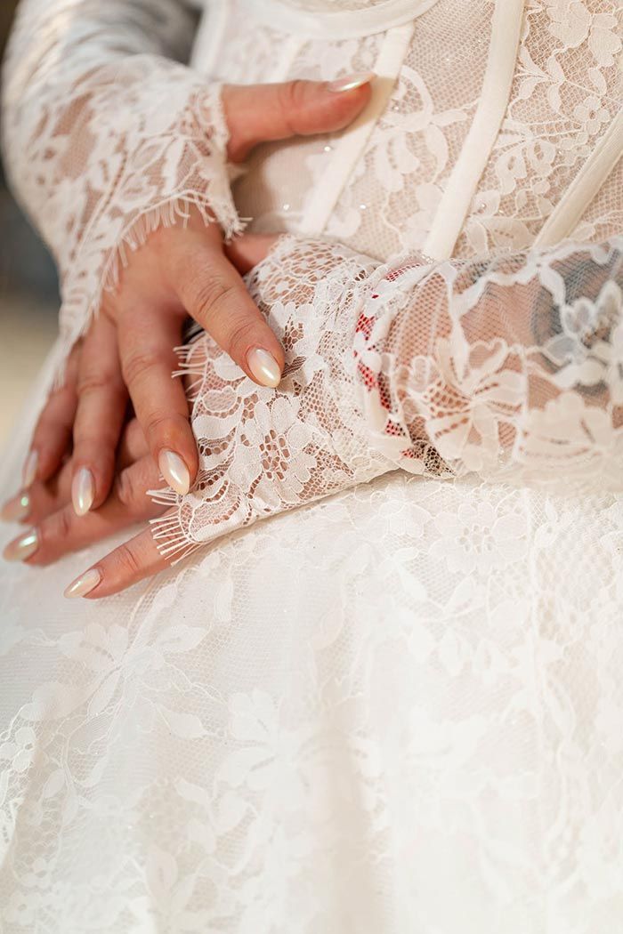 Manos de mujer unidas, vistiendo un vestido de encaje blanco con mangas largas de encaje.