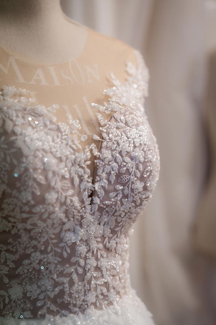 Primer plano del corpiño de un vestido de novia blanco, adornado con encaje y lentejuelas, sobre un maniquí.