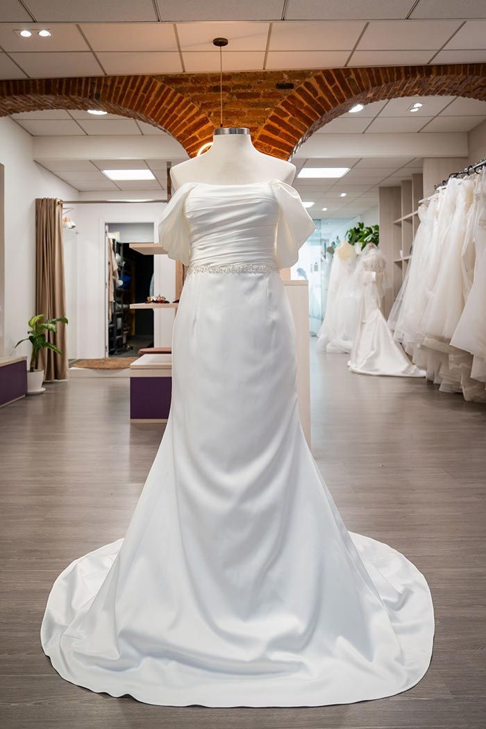 Vestido de novia sobre maniquí en tienda de novias, con falda de satén y corpiño drapeado con mangas cortas.
