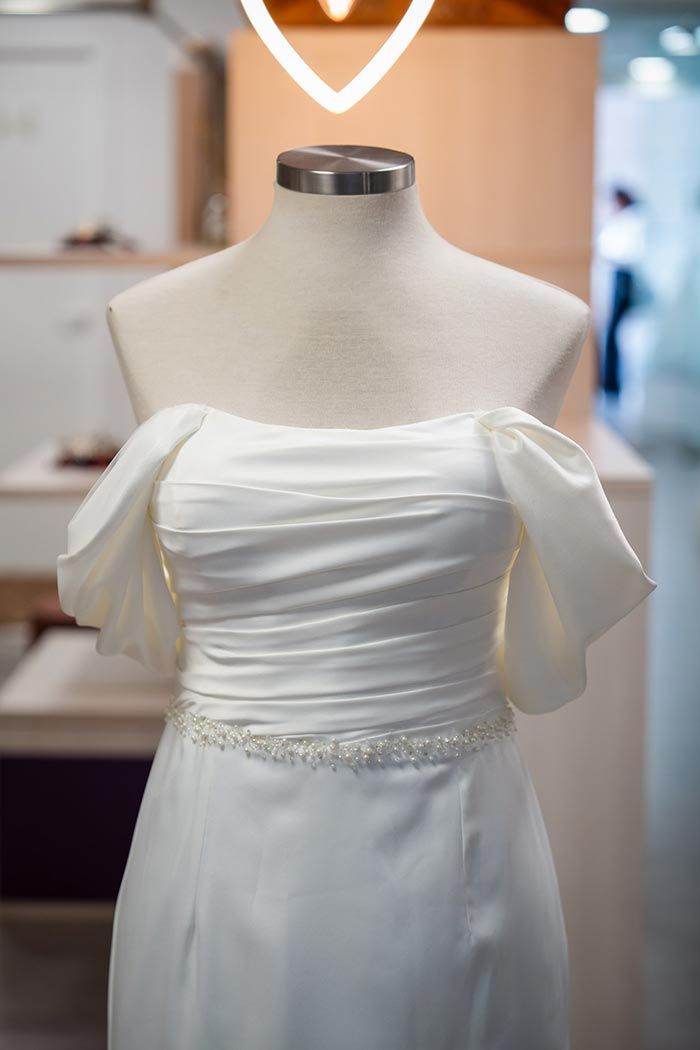 Vestido de novia blanco sobre maniquí con mangas descubiertos y cinturón de cuentas.