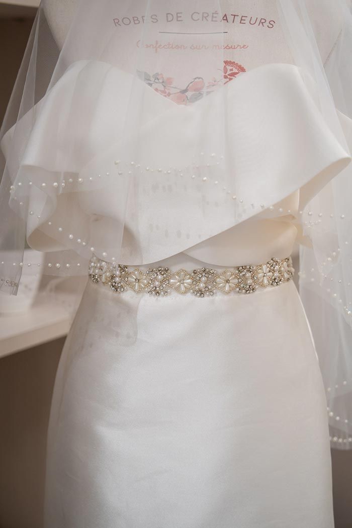 Vestido de novia blanco sobre maniquí con cinturón de cuentas y velo.