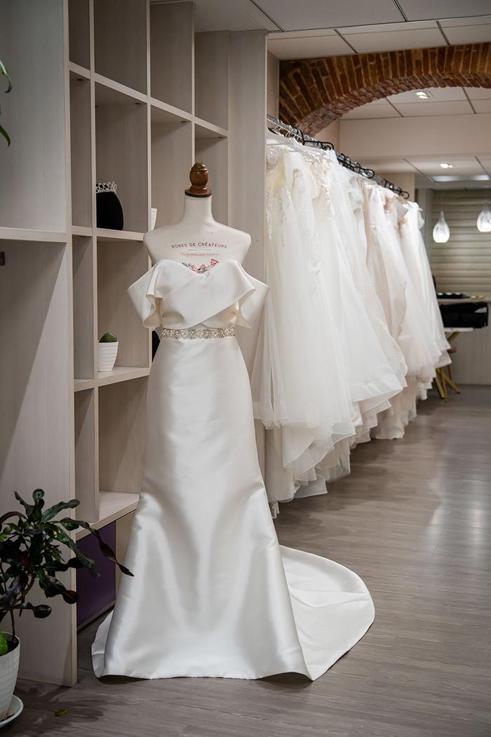 Vestido de novia en un maniquí en una tienda de novias, con otros vestidos colgados en el fondo.