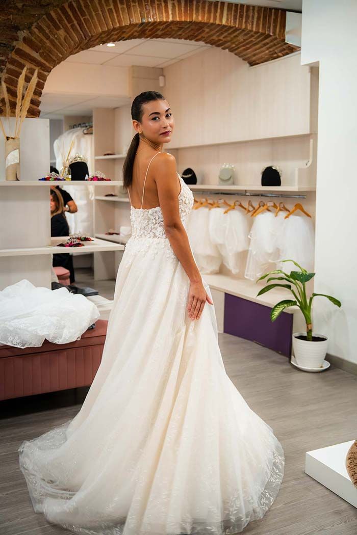 Mujer con un vestido de novia en una boutique, sosteniendo la falda y mirando por encima del hombro.