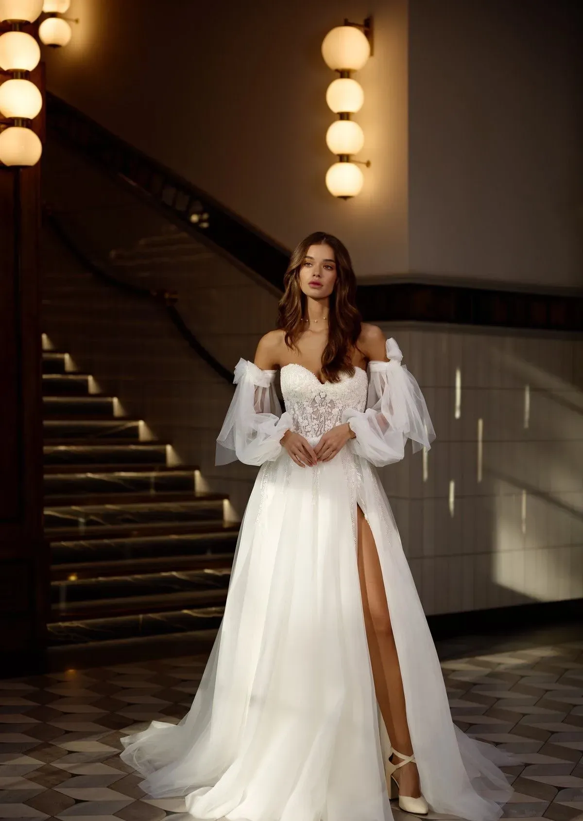 Mujer con vestido de novia con abertura alta se encuentra cerca de una escalera.