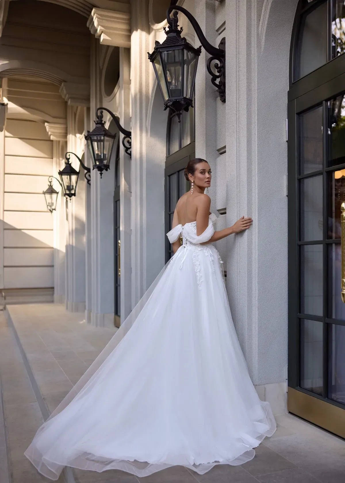 Una mujer con un vestido de novia blanco está parada en una puerta, mirando por encima del hombro.