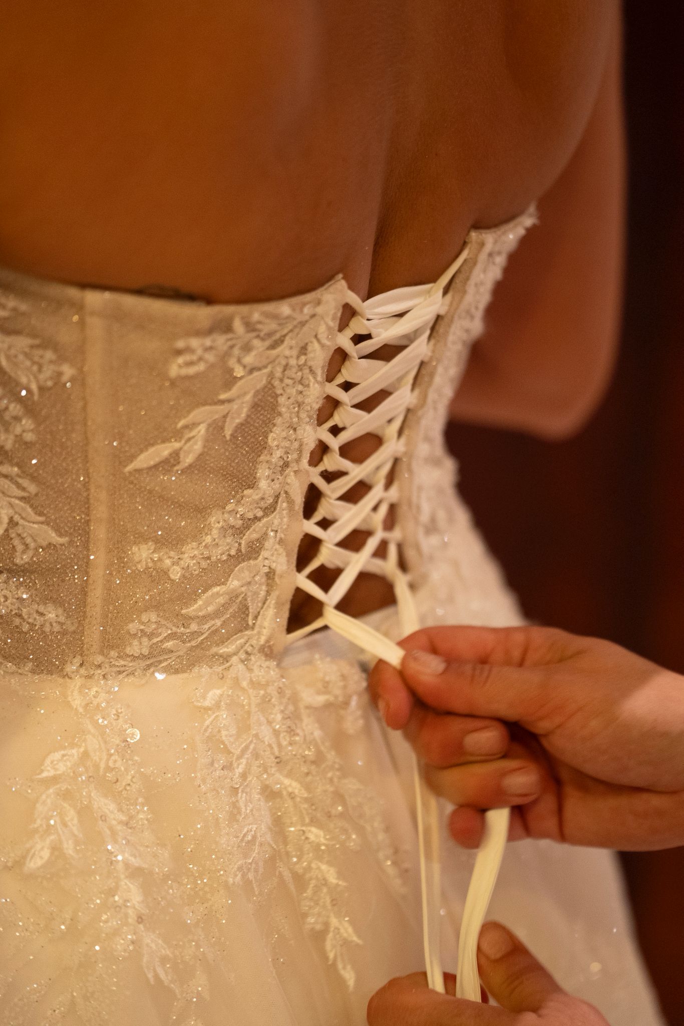 Persona con vestido de novia, con las manos atando la espalda con encaje; detalles en marfil y brillantes.